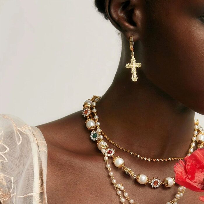 Model wearing Everette Cross Earrings in Gold with layered pearl and gemstone necklaces, close-up