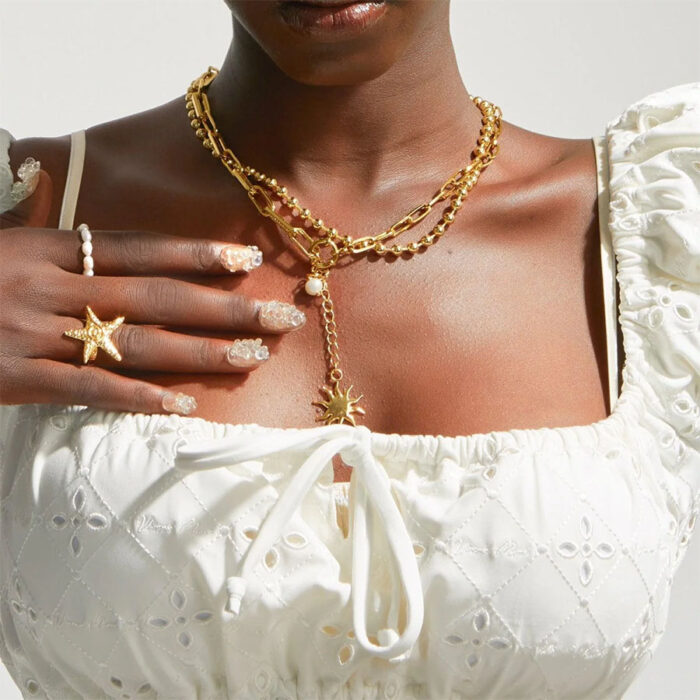 Gold Starfish Ring worn on hand with layered gold necklaces and white eyelet top