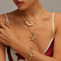 Model wearing a gold layered charm necklace with starfish pendant and baroque pearls