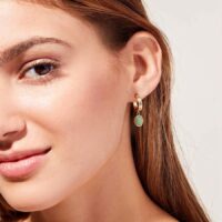Model wearing gold hoop earrings with oval green stone pendant charm