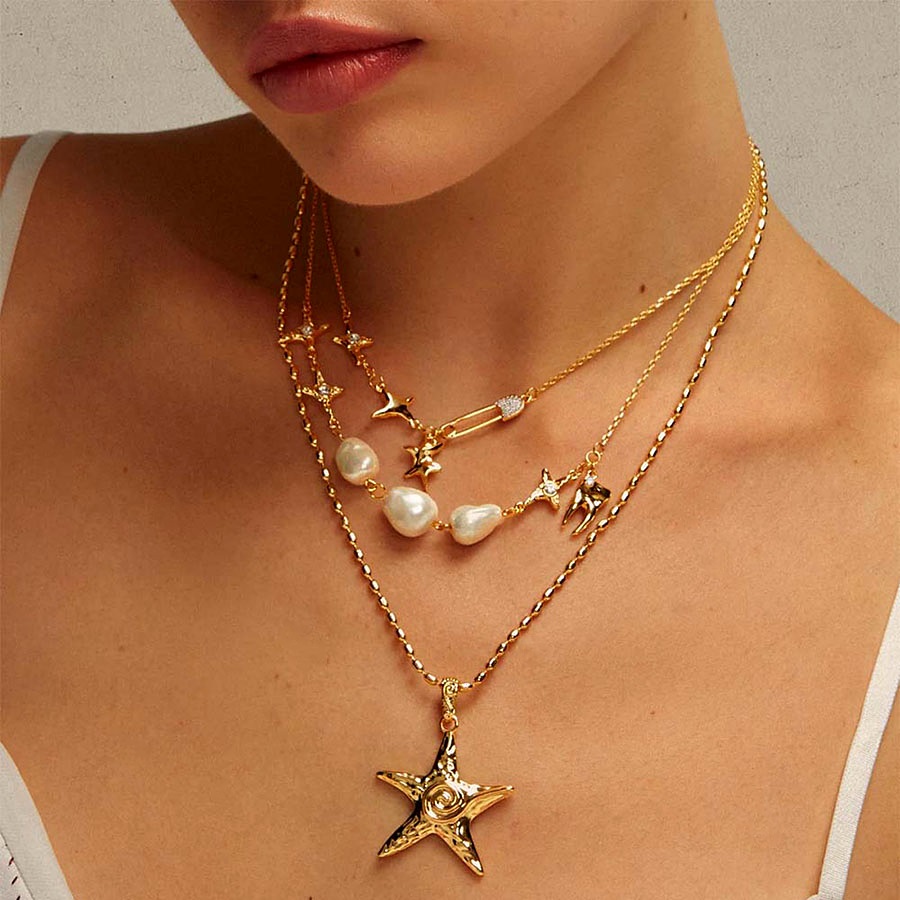 coastal chic Starfish necklace in gold layered with pearl necklace and star charms on model