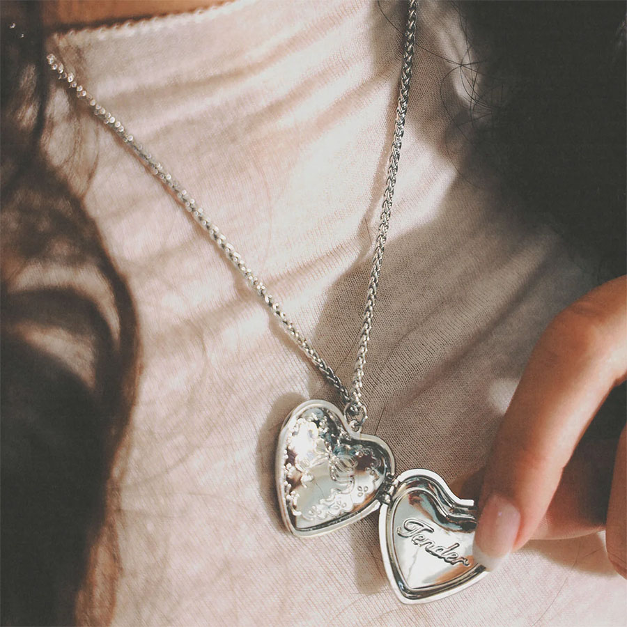 Openable heart locket necklace held in hand, open to show “Tender” engraving in a silver-tone locket