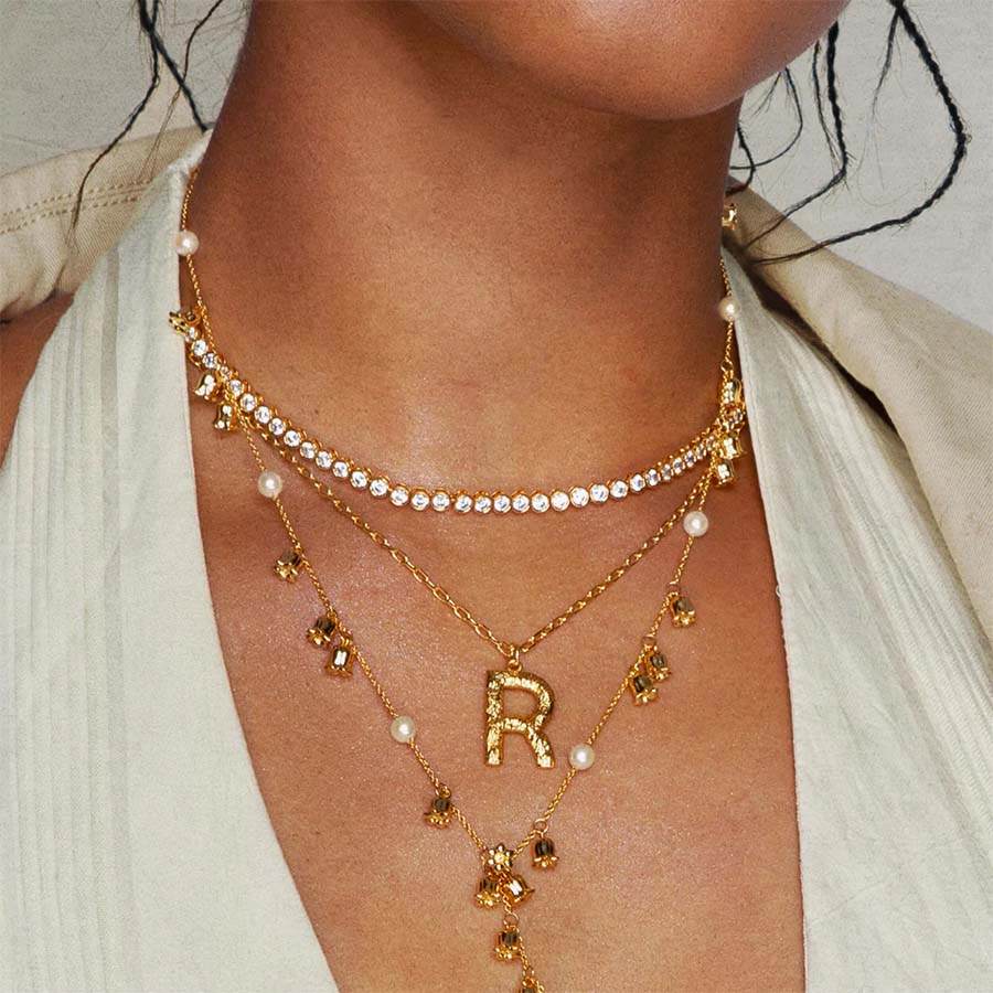 Model wearing Textured Initial Letter Necklace with molten gold initial necklace “R” layered with crystal tennis choker, Street-style Layered jewelry look